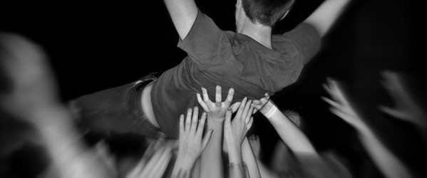 An excited young man held aloft by many hands as he crowd surfs